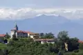 Panoramablick auf ein italienisches Bergdorf mit Kirche und Alpenpanorama.