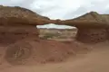 Natürliche Felsbrücke in einer Wüstenlandschaft mit roten und beigefarbenen Gesteinsformationen.