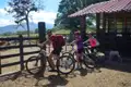 Drei Radfahrer mit Helmen und Rucksäcken machen eine Pause während ihrer Radtour an einem Gehege auf einer Farm.