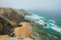 Steile Klippen und ein Sandstrand treffen auf das türkisfarbene Meer.