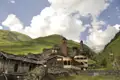 Historische Architektur eines Bergdorfes mit traditionellen Steinhäusern und Wehrtürmen inmitten einer grünen Berglandschaft.