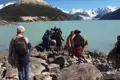 Touristen beim Ausstieg aus einem Boot an einem Gletschersee, umgeben von schneebedeckten Bergen.