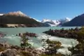 Panorama eines türkisfarbenen Sees mit Stromschnellen im Vordergrund und einer Bergkette mit schneebedeckten Gipfeln im Hintergrund.