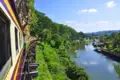 Zug auf einer hölzernen Brücke über einem Fluss in einer grünen Landschaft.