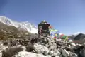 Ein Steinmal mit bunten Gebetsfahnen markiert einen Punkt im Himalaya, mit den schneebedeckten Gipfeln im Hintergrund.