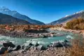 Panoramablick auf einen Fluss, der durch ein Gebirgstal fließt. Die Landschaft zeigt herbstliche Bäume und schneebedeckte Gipfel.