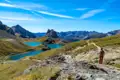 Wanderer auf einem Bergpfad inmitten einer Gebirgslandschaft mit türkisblauen Seen.