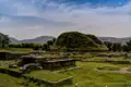 Panoramablick auf die historischen Ruinen mit einem begrasten Hügel und Bergen im Hintergrund.