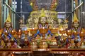 Drei goldene Mönchsstatuen mit Opfergaben und brennenden Öllampen.