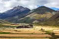Panoramablick auf goldene Felder und ein Bergdorf im Himalaya, umgeben von hohen Bergen.