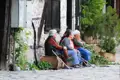 Drei ältere Frauen ruhen sich auf einer Bank vor einem Steinhaus aus.