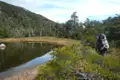 Wanderer mit Rucksack in der Nähe eines Sees und bewaldeten Hügels.