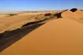 Ausgedehnte Sanddünenlandschaft mit spärlicher Vegetation unter einem klaren blauen Himmel.