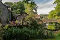 Steinhaus mit Terrasse am Flussufer und eine historische Steinbrücke.