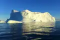 Wanderer auf einem Felsen mit Blick auf zahlreiche Eisberge im Meer.