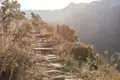 Steinerner Wanderweg in den Bergen, umgeben von trockener Vegetation und Kakteen.
