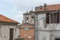 Kirchturm mit Uhr und Glocke inmitten von Häusern mit Terrakottadächern in einem italienischen Dorf.