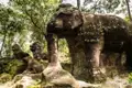 Alte steinerne Elefanten- und Löwenstatuen, umgeben von üppiger Vegetation.