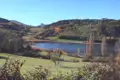 Blick auf einen See in einer hügeligen Landschaft im Herbst.