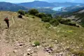 Wanderer auf einem steinigen Bergpfad mit Blick auf einen See und Berglandschaft im Hintergrund.