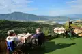 Zwei Personen frühstücken auf einer Terrasse mit Blick auf einen See und Berge im Hintergrund.