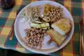 Teller mit verschiedenen Speisen: Gegrillte Zucchini, Bohnensalat, Kichererbsen, Omelett, geriebenes Gemüse und Brot.