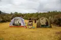 Zeltplatz mit vorbereitetem Essen und grasenden Pferden im Hintergrund.