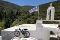 E-Bike vor einer weißen Kapelle in den griechischen Bergen. Eine griechische Flagge ist zu sehen.