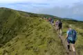 Wandergruppe auf einem Pfad entlang eines grünen Hügels.