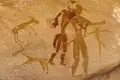 Historische Felsmalerei mit Darstellung von zwei menschlichen Figuren und mehreren Tieren, die wahrscheinlich Antilopen sind.