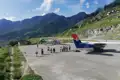 Zwei Flugzeuge auf einem Bergflughafen, umgeben von Passagieren und Gepäck.