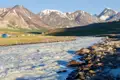 Schneebedeckte Berge, ein schnell fließender Fluss und ein Basislager im Vordergrund.