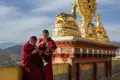 Zwei Mönche spielen traditionelle Instrumente vor einer goldenen Statue mit Dharma-Rad und Hirschen, die einen wichtigen Aspekt des buddhistischen Glaubens symbolisieren.