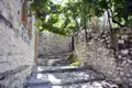 Steinmauern und Treppen in einer Gasse, überdacht von Weinreben.