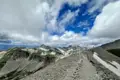 Panoramablick von einem Berggipfel auf eine Bergkette mit einem felsigen Pfad und Schneefeldern.