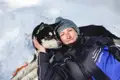 Person kuschelt mit Husky im Schnee.