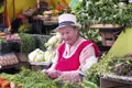 Marktfrau mit Hut verkauft frisches Gemüse und Kräuter.