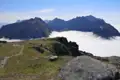 Blick von einem Bergplateau auf ein Wolkenmeer und umliegende Bergketten.