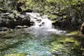 Person badet in einem klaren Flussbecken unter einem Wasserfall.
