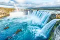 Panoramablick auf einen mehrstufigen Wasserfall mit türkisfarbenem Wasser und einem Regenbogen.