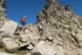 Zwei Wanderer erklimmen einen felsigen Bergpfad, markiert mit rot-weißen Wegzeichen.