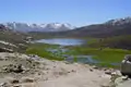Panoramablick auf einen Bergsee mit schneebedeckten Gipfeln im Hintergrund.