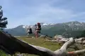 Zwei Wanderer mit Trekkingstöcken und großen Rucksäcken wandern auf einem Bergpfad. Im Hintergrund sind schneebedeckte Berggipfel zu sehen.