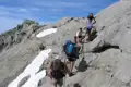 Wanderer auf einem anspruchsvollen Bergpfad mit Schneeresten.