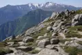 Wanderweg mit Felsen und Vegetation, im Hintergrund schneebedeckte Bergspitzen.