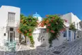 Traditionelle Architektur einer griechischen Inselgasse mit weiß getünchten Häusern, blühenden Pflanzen und einer blau-weißen Kirche.
