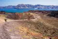 Wanderer auf einem vulkanischen Pfad mit Blick auf die Caldera und Kreuzfahrtschiffe im Hintergrund.