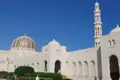 Sultan-Qabus-Moschee mit goldener Kuppel und Minarett unter blauem Himmel.