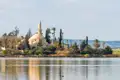 Hala-Sultan-Tekke-Moschee mit dem Salzsee im Vordergrund und Windkraftanlagen in der Ferne.