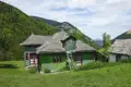 Grünes Haus mit Schindeldach und Leiter in einer bergigen Landschaft.